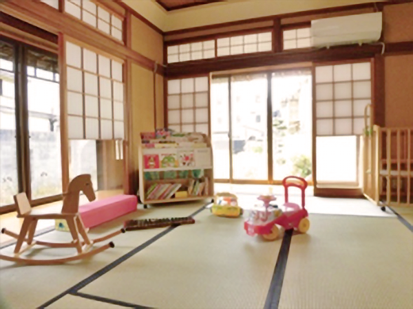 ベビーベッドやおもちゃ、絵本などがある窓付きの和室の写真